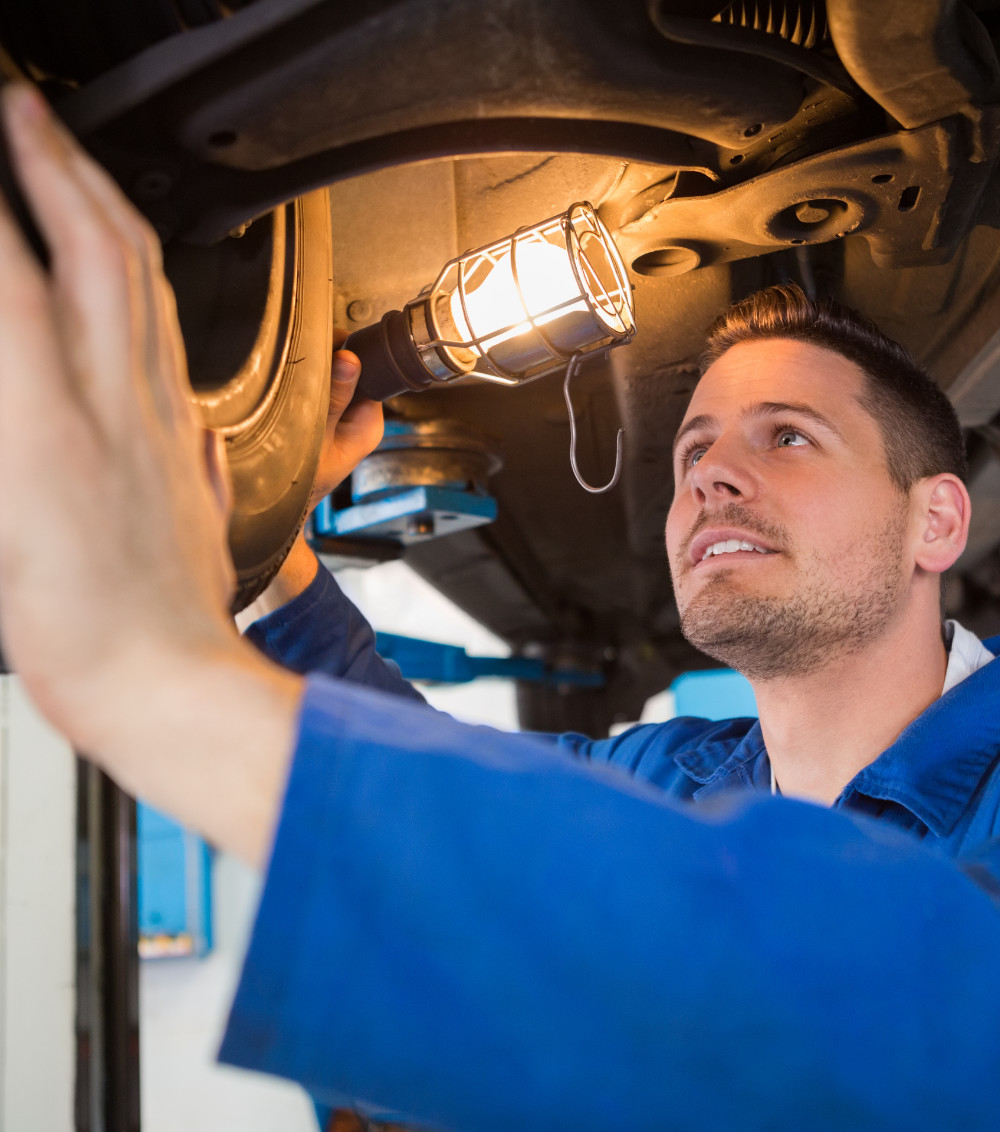 Mechanic using torch to look under car at the repair garage - MOT Leighton Buzzard